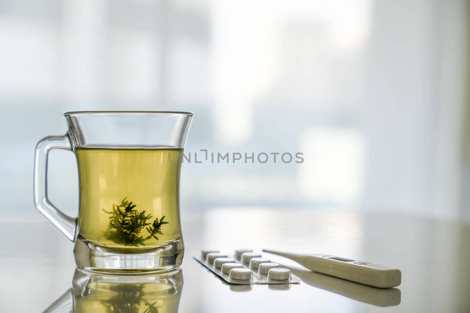 Glass transparent cup with herbal tea and grass leaves, thermometer, tablets. Concept of health treatment by Laguna781