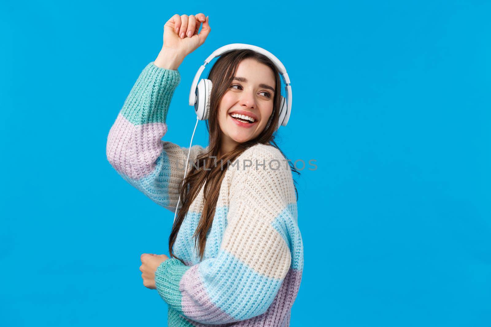 Waist-up portrait carefree, happy dancing woman in headphones, smiling raising hands up free and upbeat, enjoying favorite songs, special winter holidays playlisty, laughing joyfully, blue background.