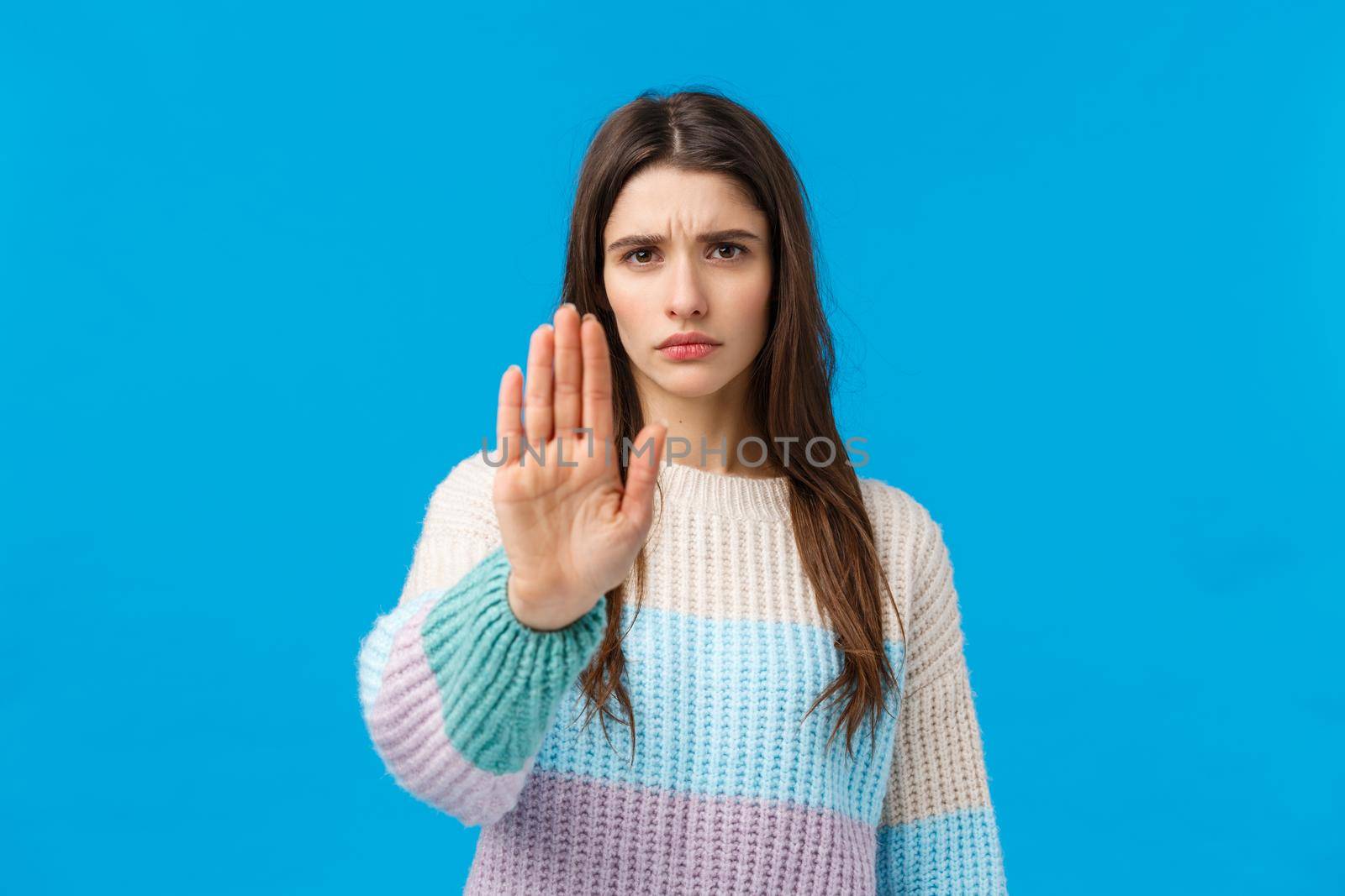 Quit it, enough. Displeased serious and fed up young assertive girl, showing stop gesture, raise palm and frowning disapproval, refuse, prohibit and disagree, standing blue background by Benzoix