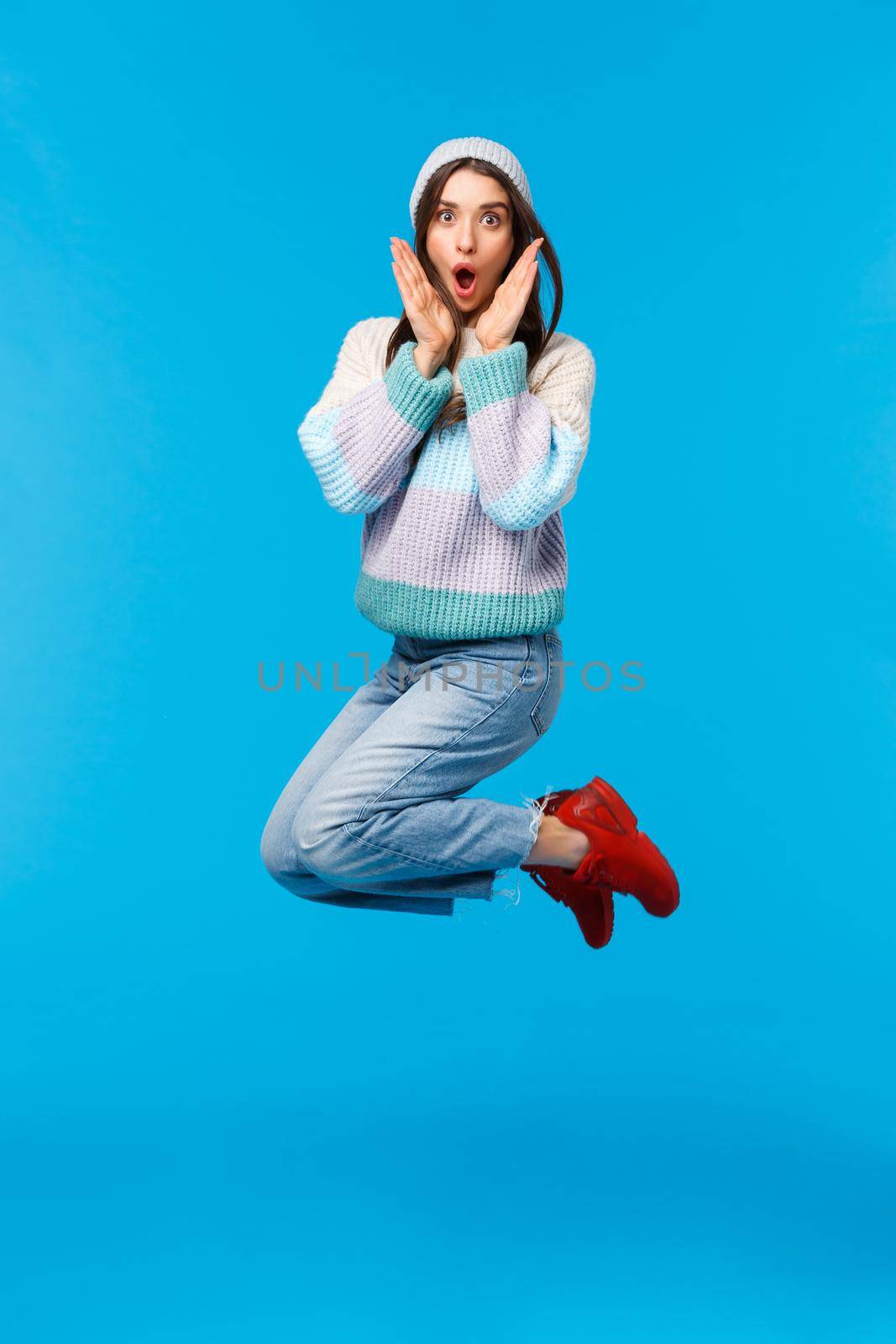 Full-length vertical shot surprised cute girl astonished how many gifts under christmas tree, shocked with super big discounts, winter shopping season, jumping and look amazed camera, blue background.