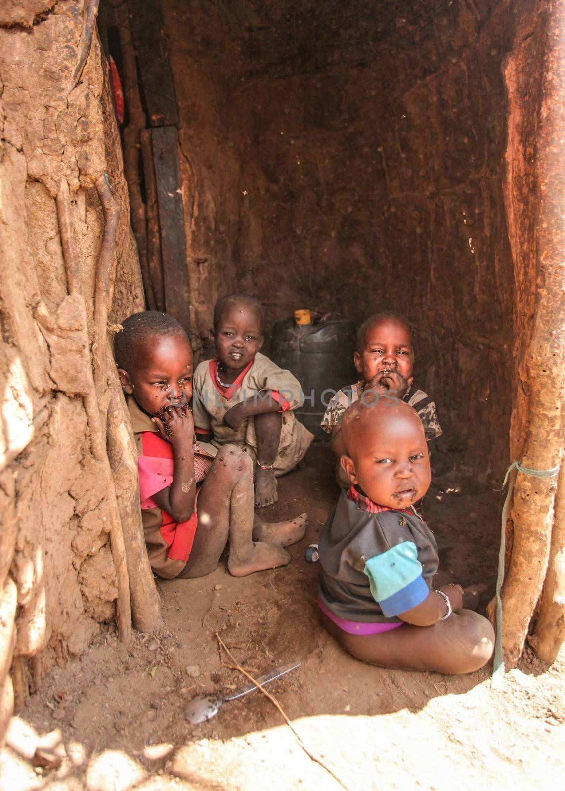 Unknown Masai village near Amboselli park, Kenya - April 02, 2015: Group of poor dirty children with faces and mouth covered with flies sitting at entrance to their hut.