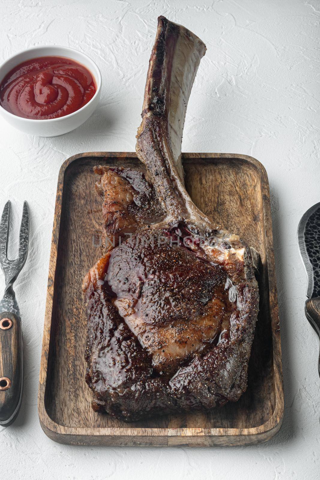Steak on the bone. tomahawk steak freshly grilled dry aged BBQ food set, on wooden serving board, on white stone background