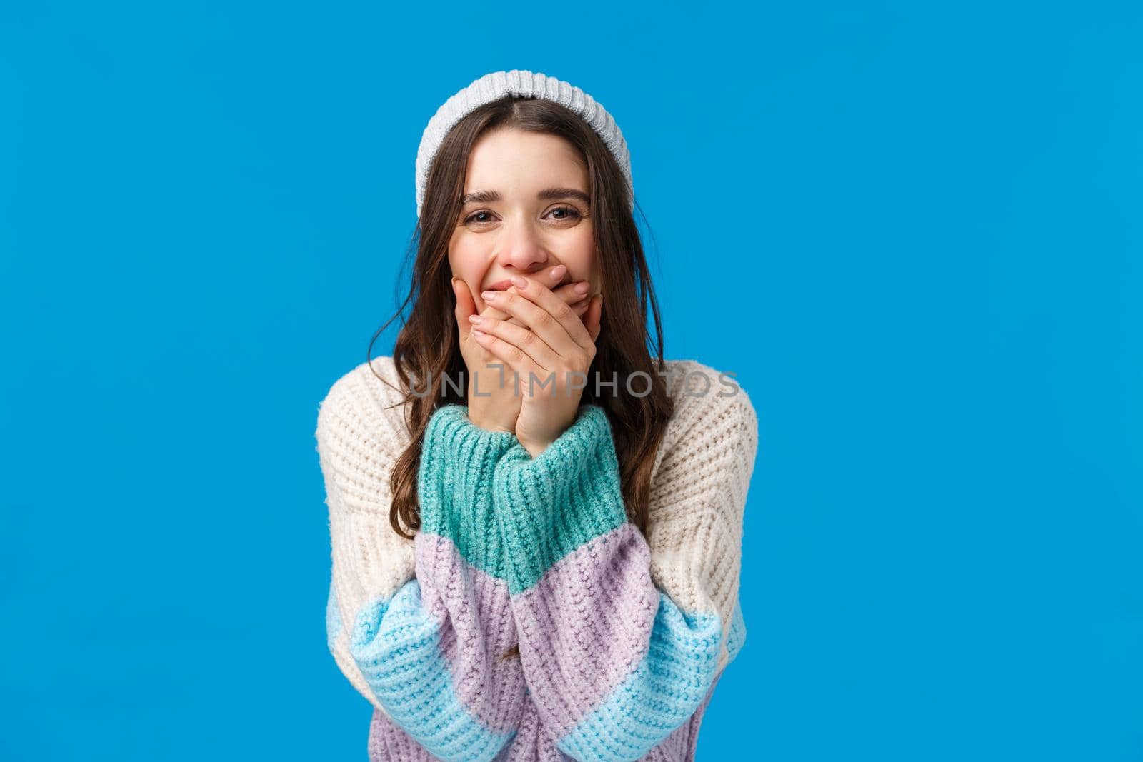 Emotions, new year, winter holidays concept. Cheerful charismatic feminine young woman laughing out loud, chuckle and shut mouth with hands, giggle over something funny, blue background.
