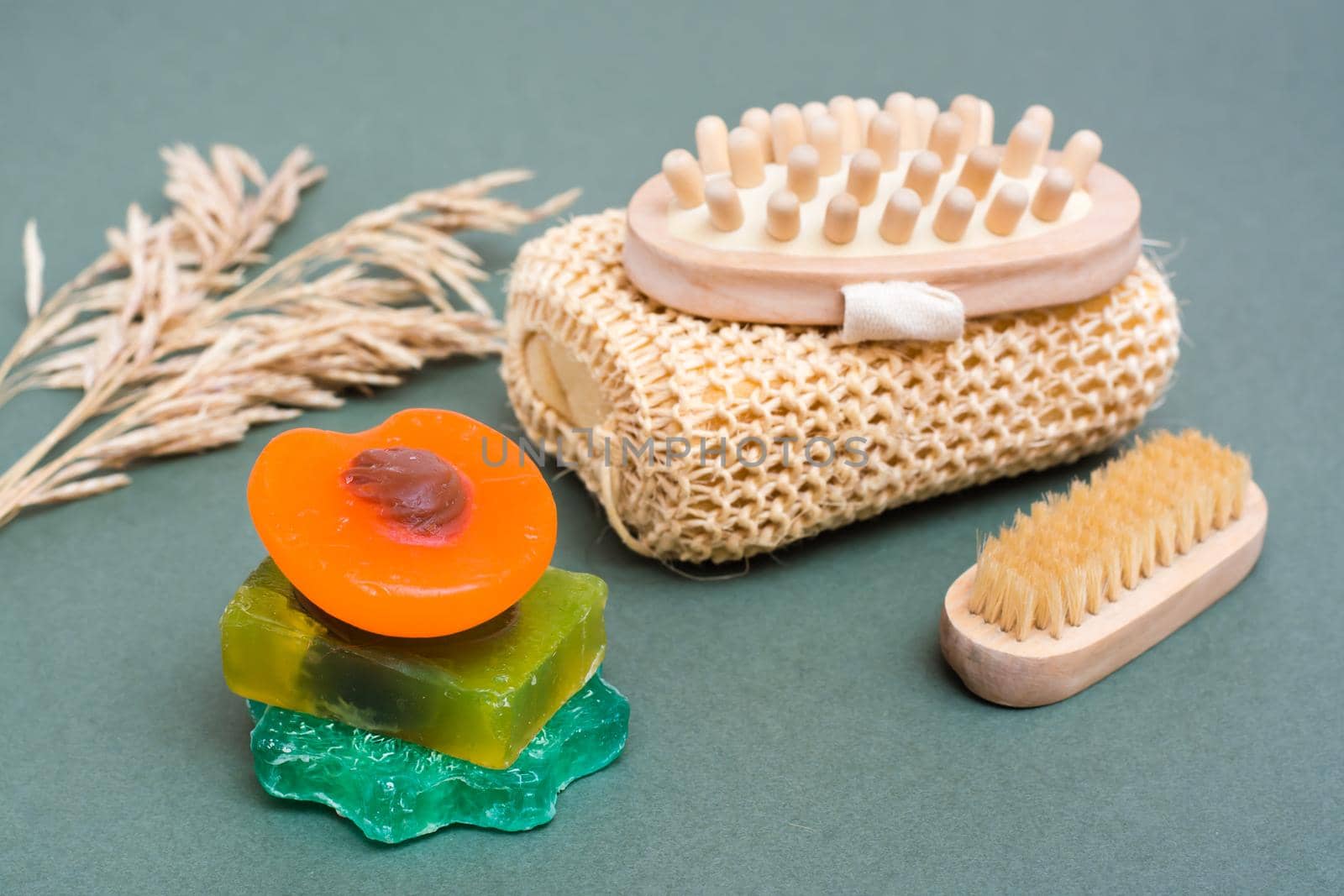 Body care. Different types of handmade soap without additives, washcloth, massager and brush on a green background.