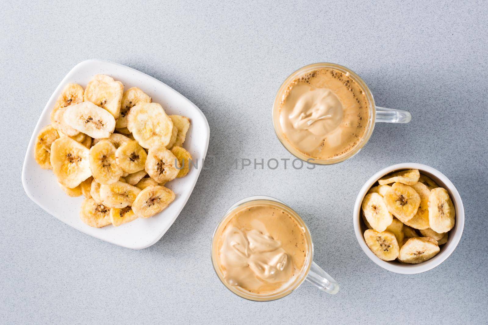 Quarantine trendy cuisine. Two cups with dalgona coffee and banana chips on a gray background. Top view