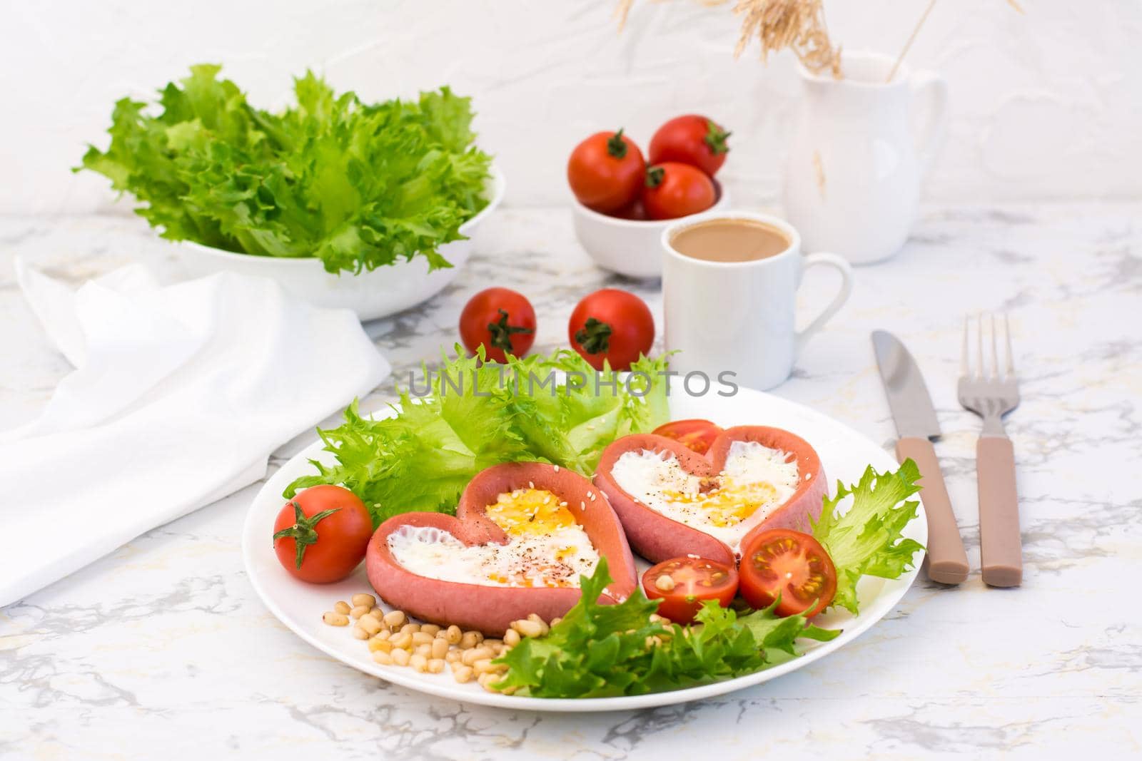Romantic breakfast. Fried eggs in heart shaped sausages, lettuce and cherry tomatoes on a plate on the table
