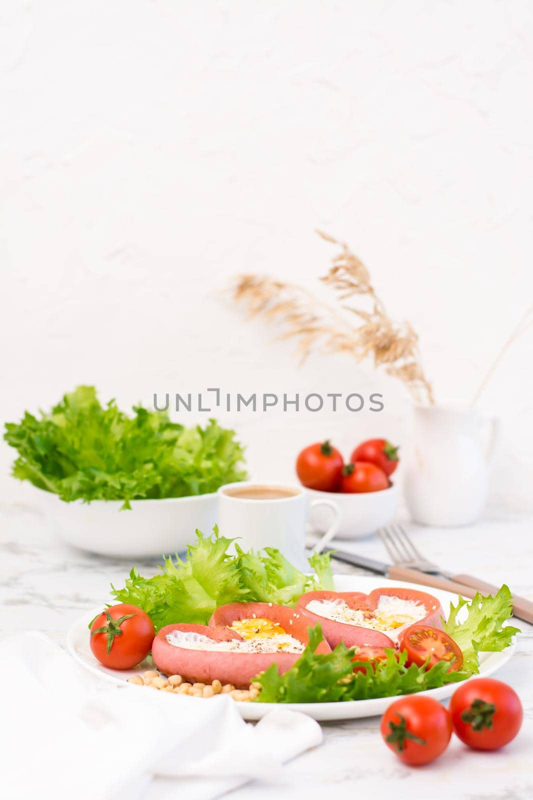 Romantic breakfast. Fried eggs in heart shaped sausages, lettuce and cherry tomatoes on a plate on the table. Vertical view. Copy space by Aleruana