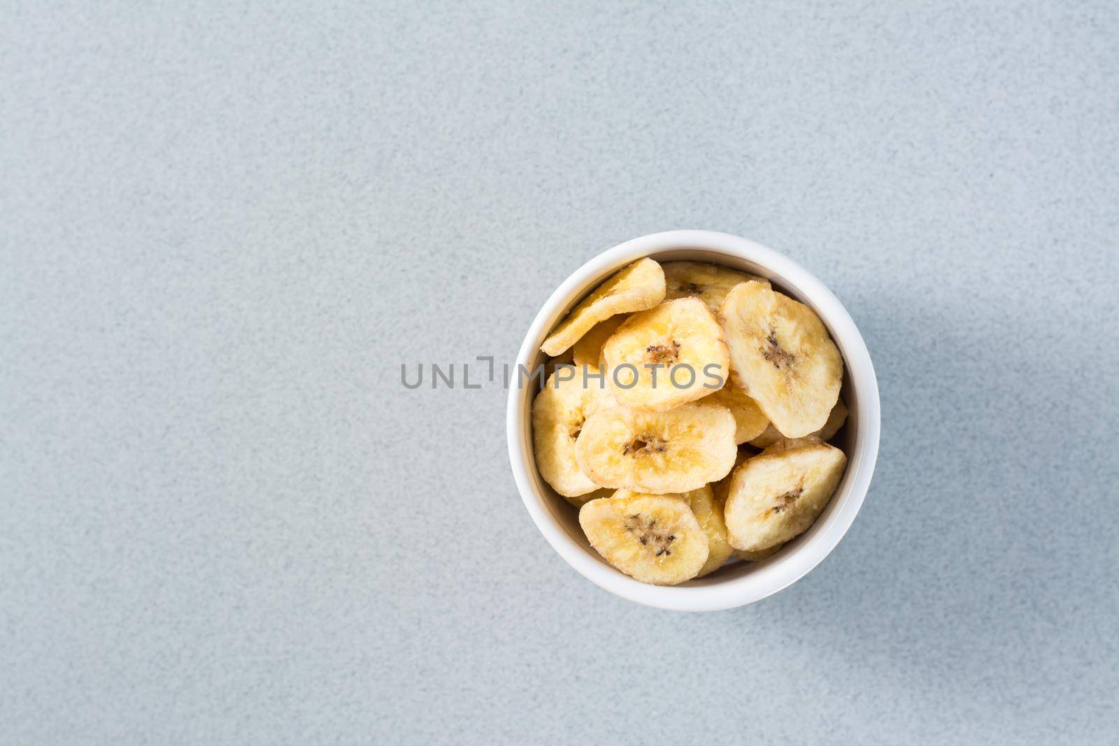 Baked banana chips in a white bowl on the table. Fast food. Copy space. Top view
