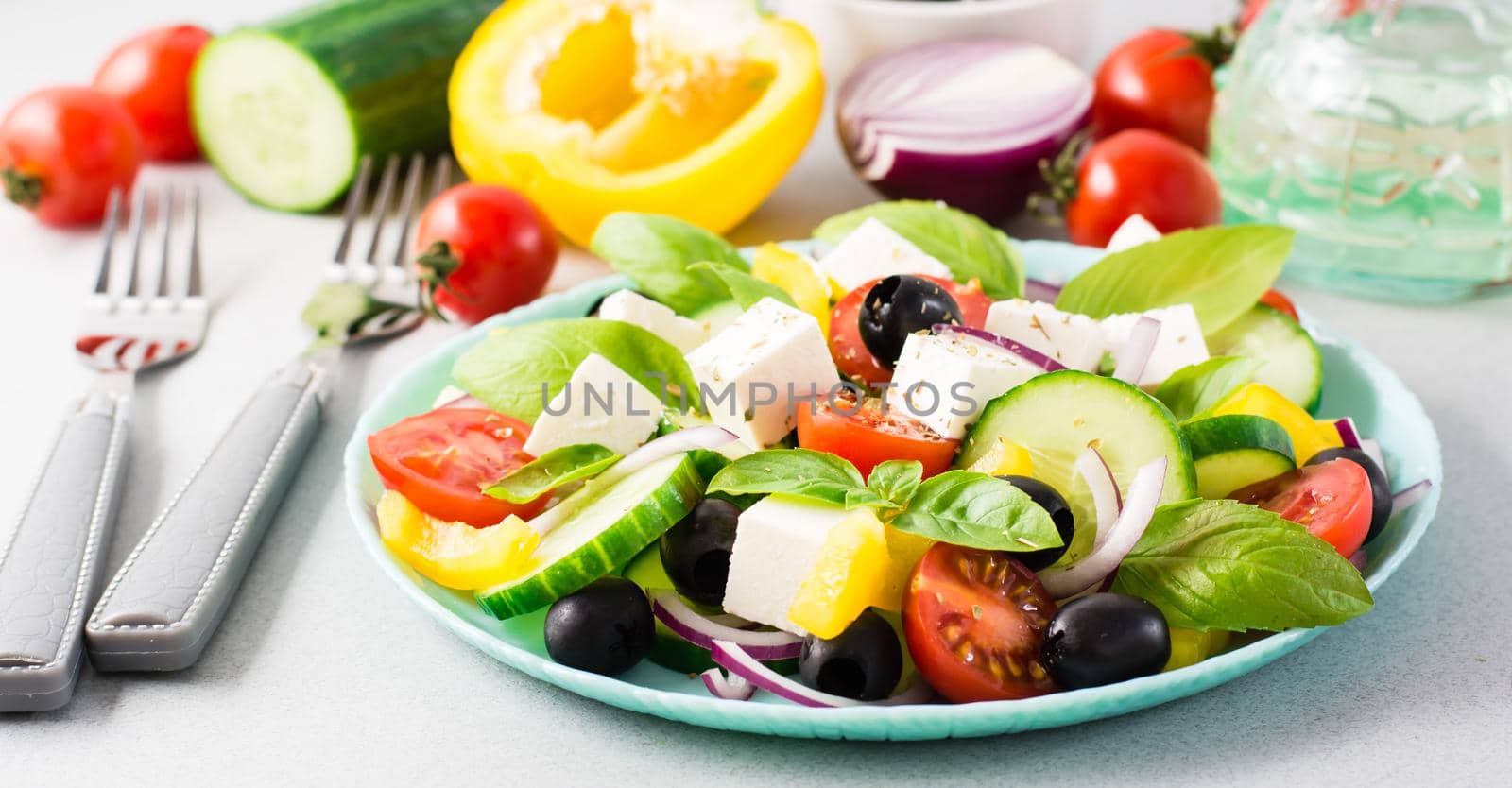 Fresh homemade greek salad with basil leaves on a plate and ingredients for cooking on the table. Domestic life. Web banner by Aleruana
