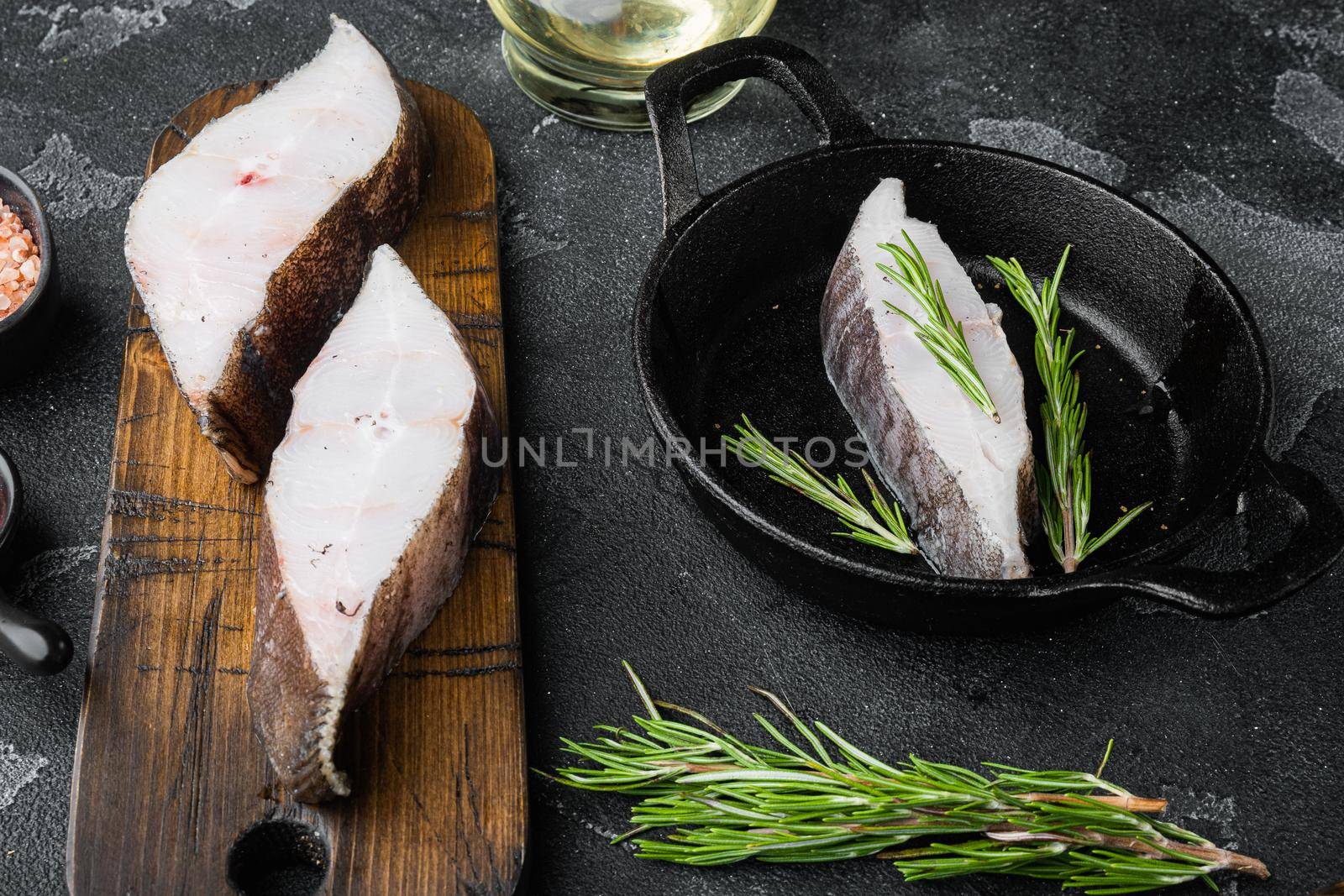 Raw halibut set, with ingredients and rosemary herbs, on black dark stone table background