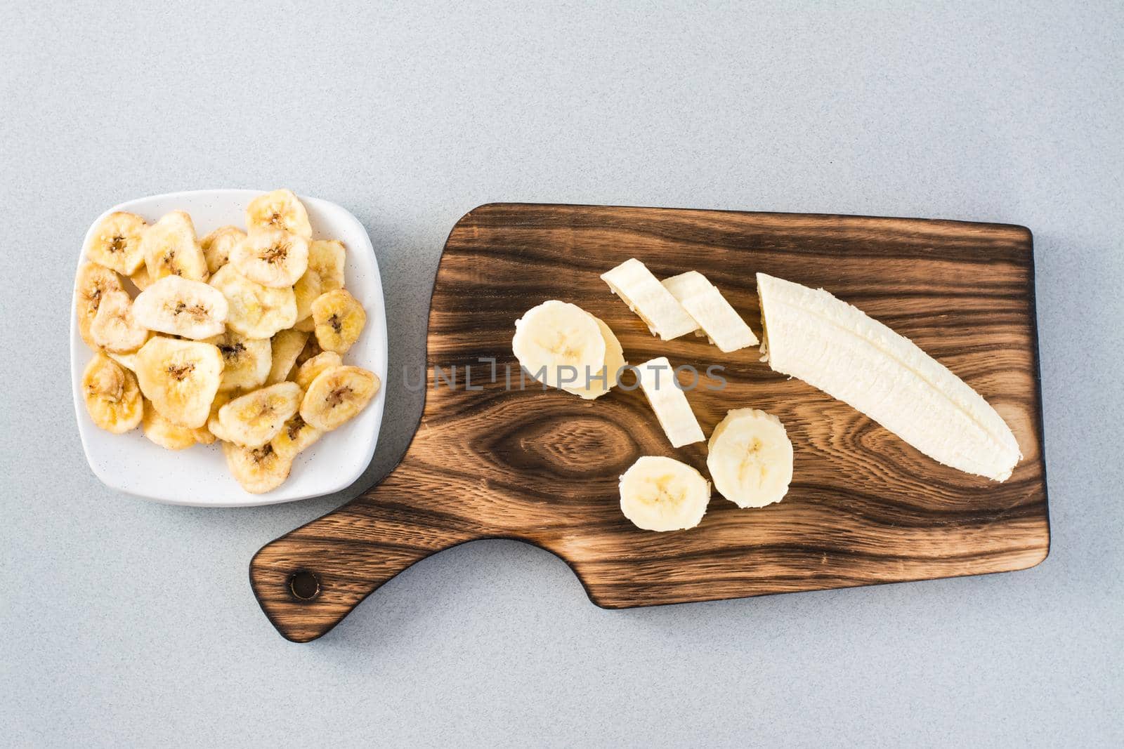 Banana slices on a cutting board and banana chips on a saucer on the table. Fast food.