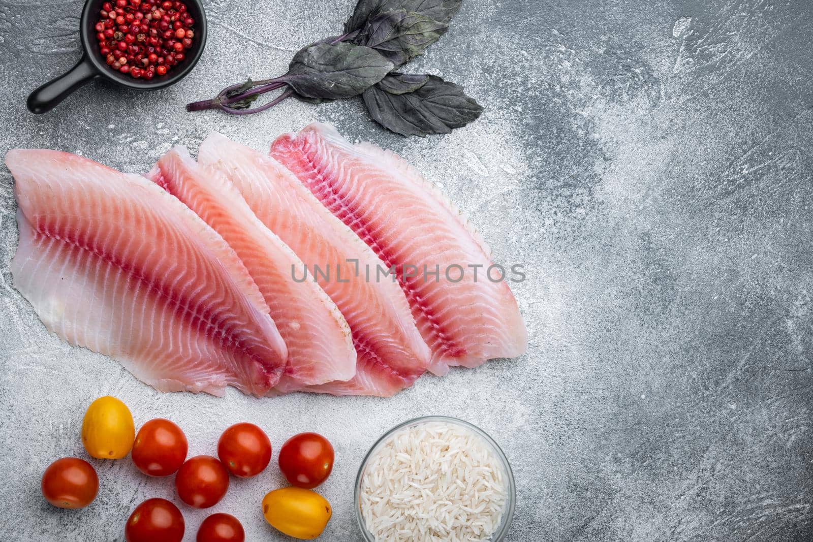 Raw white fish tilapia, with basmati rice and cherry tomatoes ingredients, on gray background, top view with copy space for text