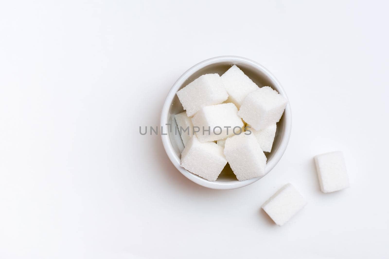 White sugar cubes in a bowl on a white background. Top view