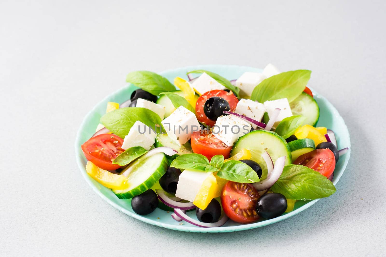 Fresh homemade greek salad with basil leaves on a plate on the table. Domestic life by Aleruana
