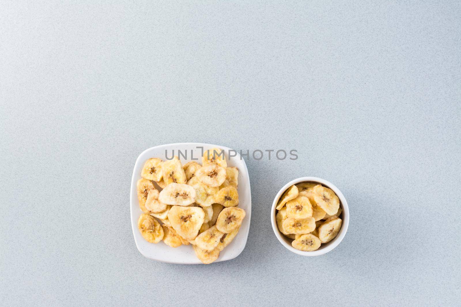 Baked banana chips in a white bowl and saucer on the table. Fast food. Web banner. Top view. Close-up