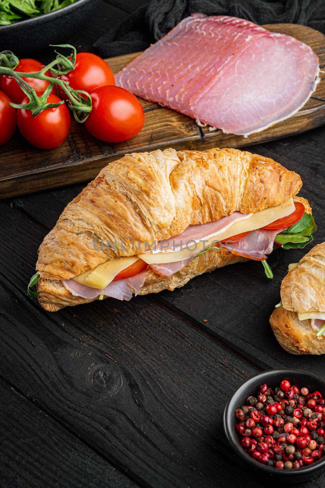 Fresh croissant or sandwich with salad, ham, jamon, prosciutto set, with herbs and ingredients, on black wooden table background, with copy space for text
