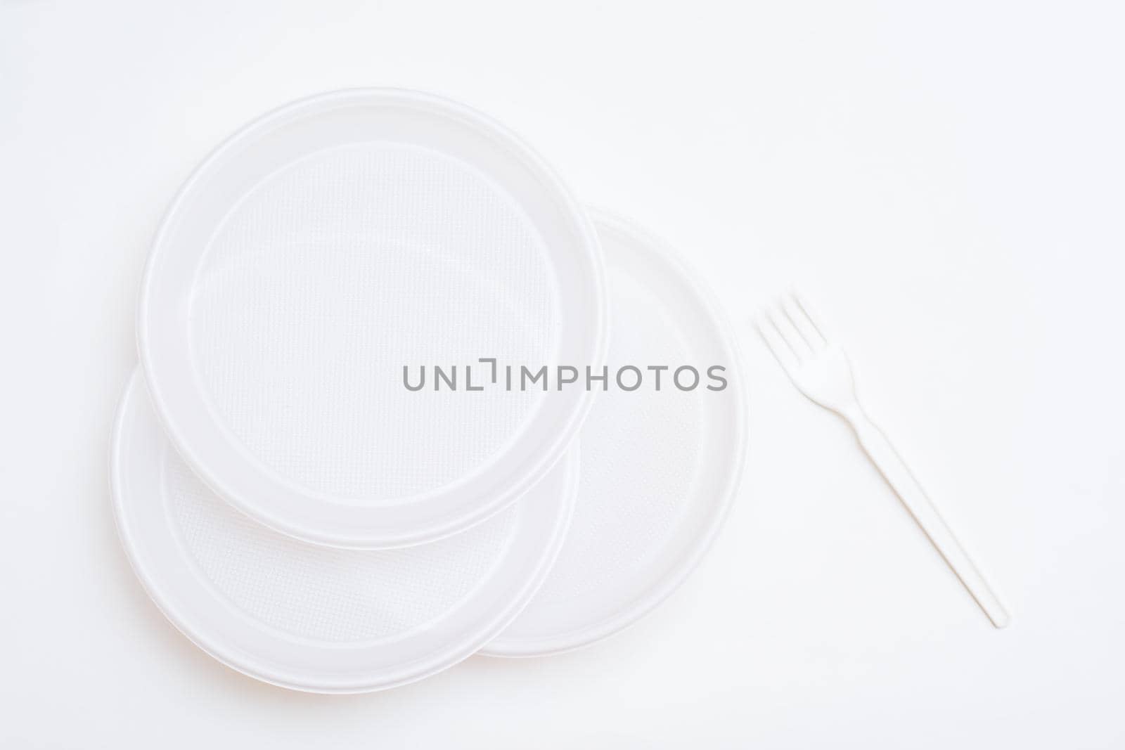 Three white disposable clean plastic plates and a fork on a white background. Top view