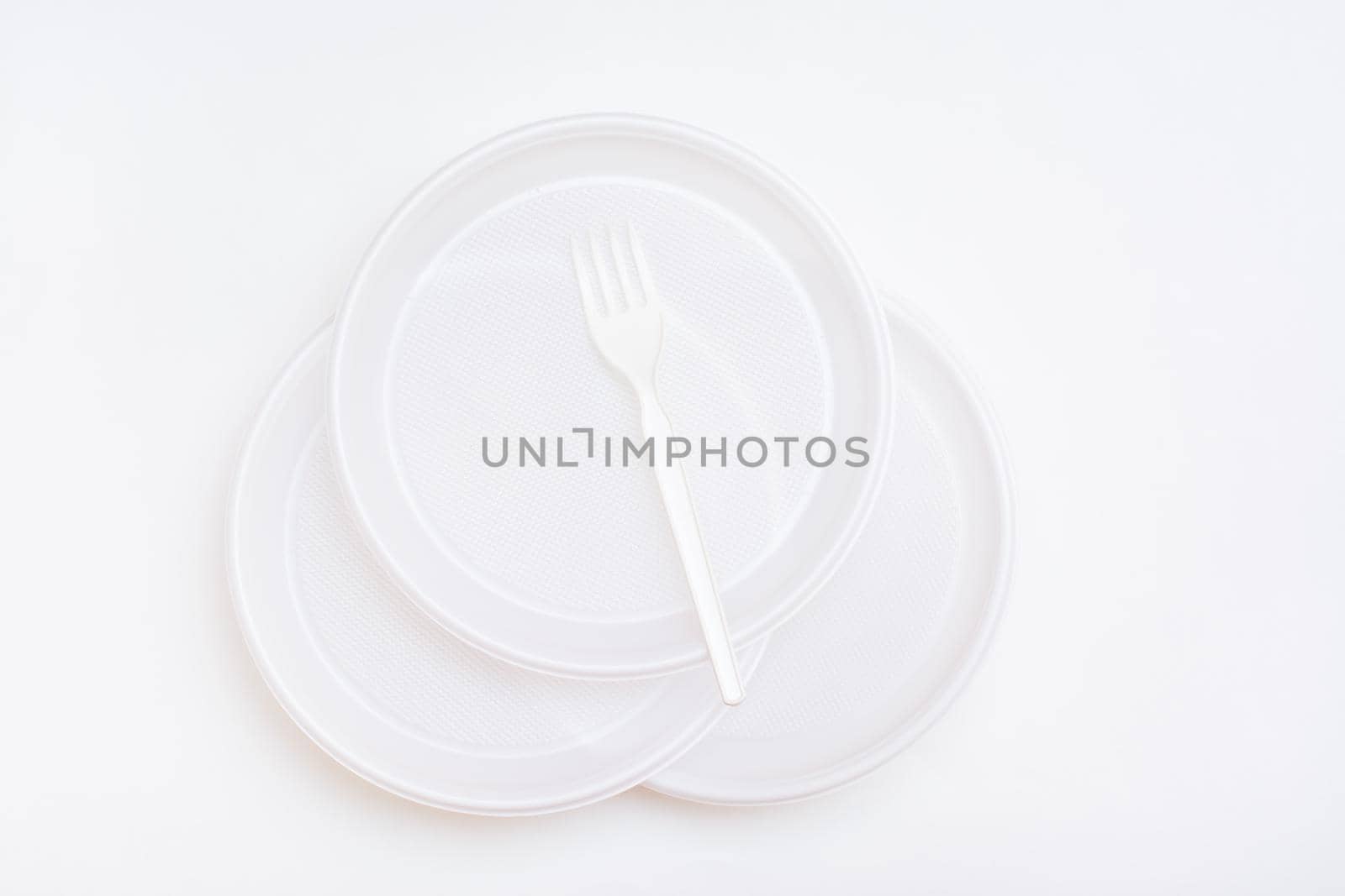 Three white disposable clean plastic plates and a fork on them on a white background. Top view by Aleruana