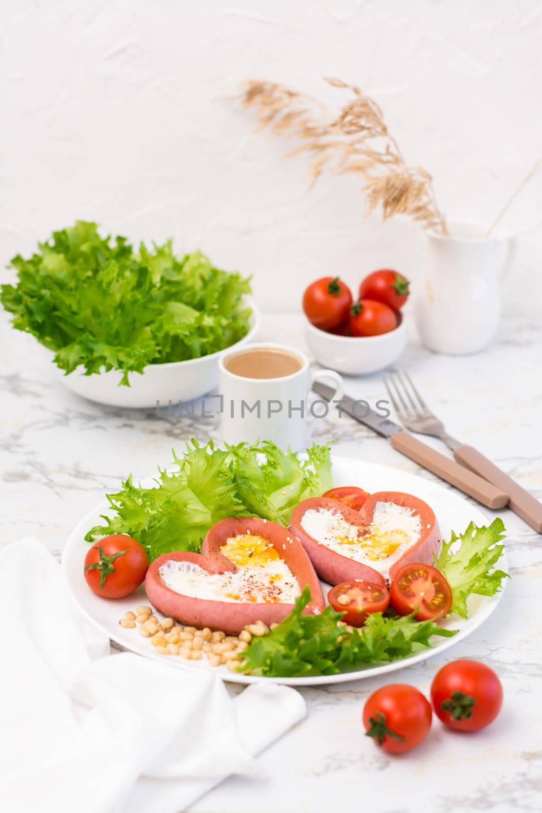 Romantic breakfast. Fried eggs in heart shaped sausages, lettuce and cherry tomatoes on a plate on the table. Vertical view by Aleruana