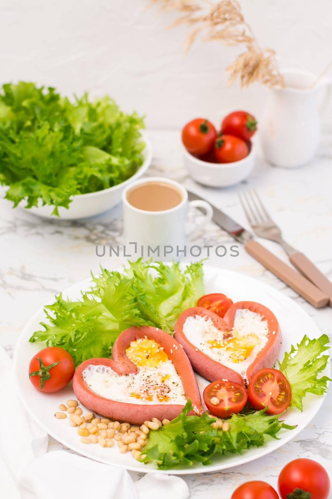 Love breakfast. Fried eggs in heart shaped sausages, lettuce and cherry tomatoes on a plate and a cup of coffee on the table. Vertical view
