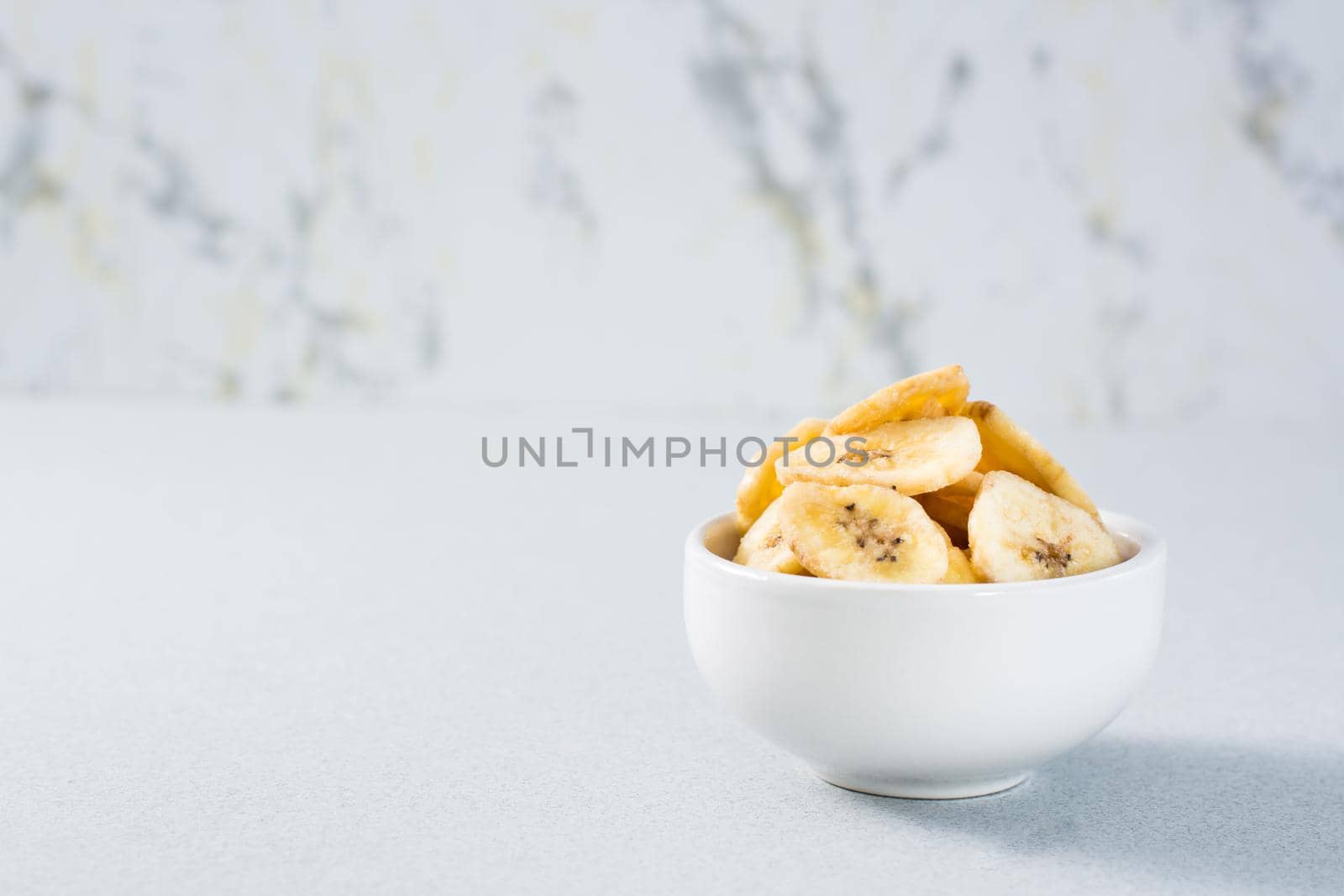 Banana chips in a bowl on the table. Fast food. Copy space by Aleruana