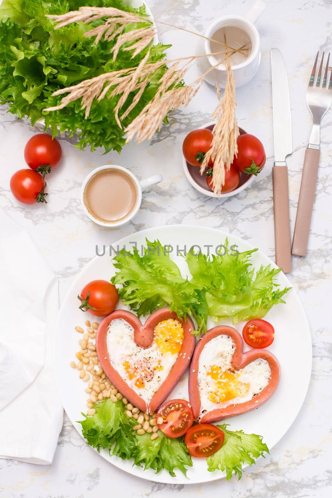 Romantic breakfast. Fried eggs in heart shaped sausages, lettuce and cherry tomatoes on a plate on the table. Top and vertical view