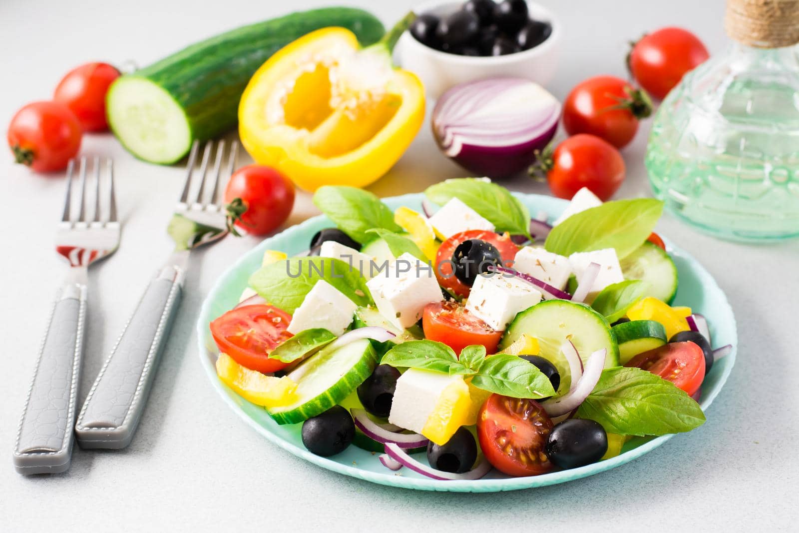 Fresh homemade greek salad with basil leaves on a plate and ingredients for cooking on the table. Domestic life by Aleruana