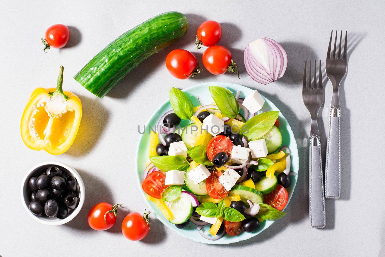 Fresh homemade greek salad with basil leaves on a plate and ingredients for cooking on the table. Domestic life. Top view. Hard light by Aleruana