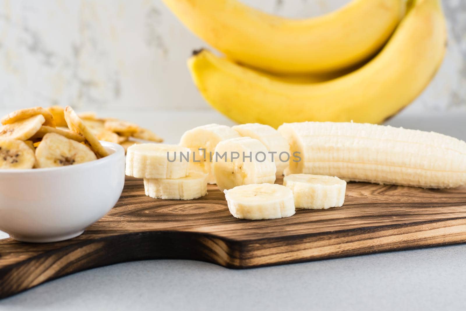 Banana slices on a cutting board and banana chips in a bowl on the table. Fast food.
