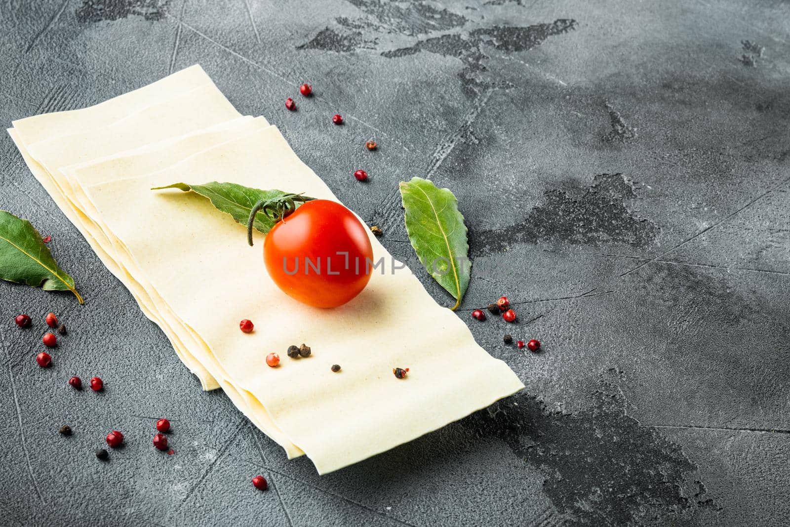 Uncooked lasagna sheets set, with seasoning and herb, on gray stone background, with copy space for text
