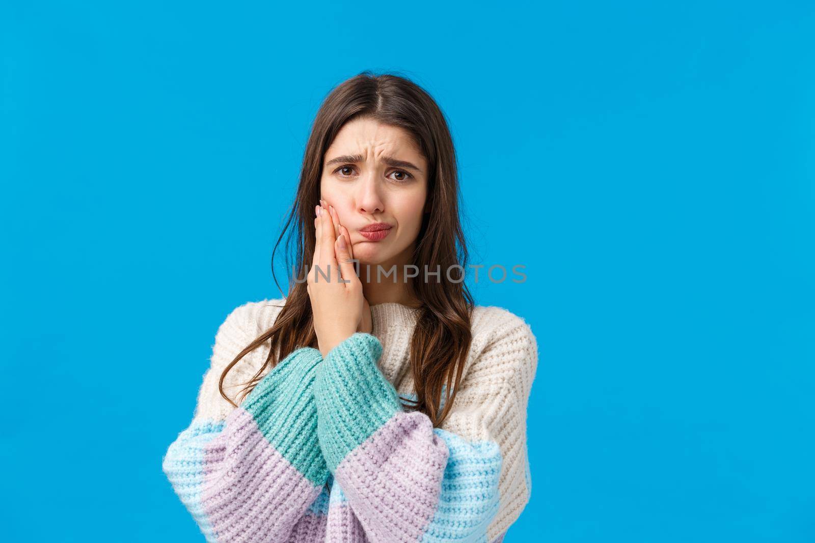 Health, stomatology concept. Silly cute woman in winter sweater, complaining on toothache, having decay or rotten tooth, touching cheek frowning and sulking from pain, waiting in dentist office.