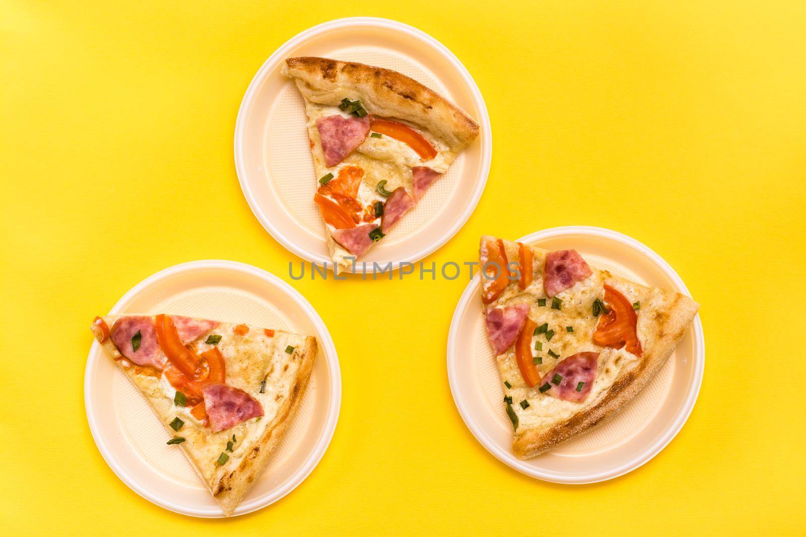 Takeaway and delivery. Three pieces of pizza in disposable plastic plates on a yellow background. Lunch for a group of friends