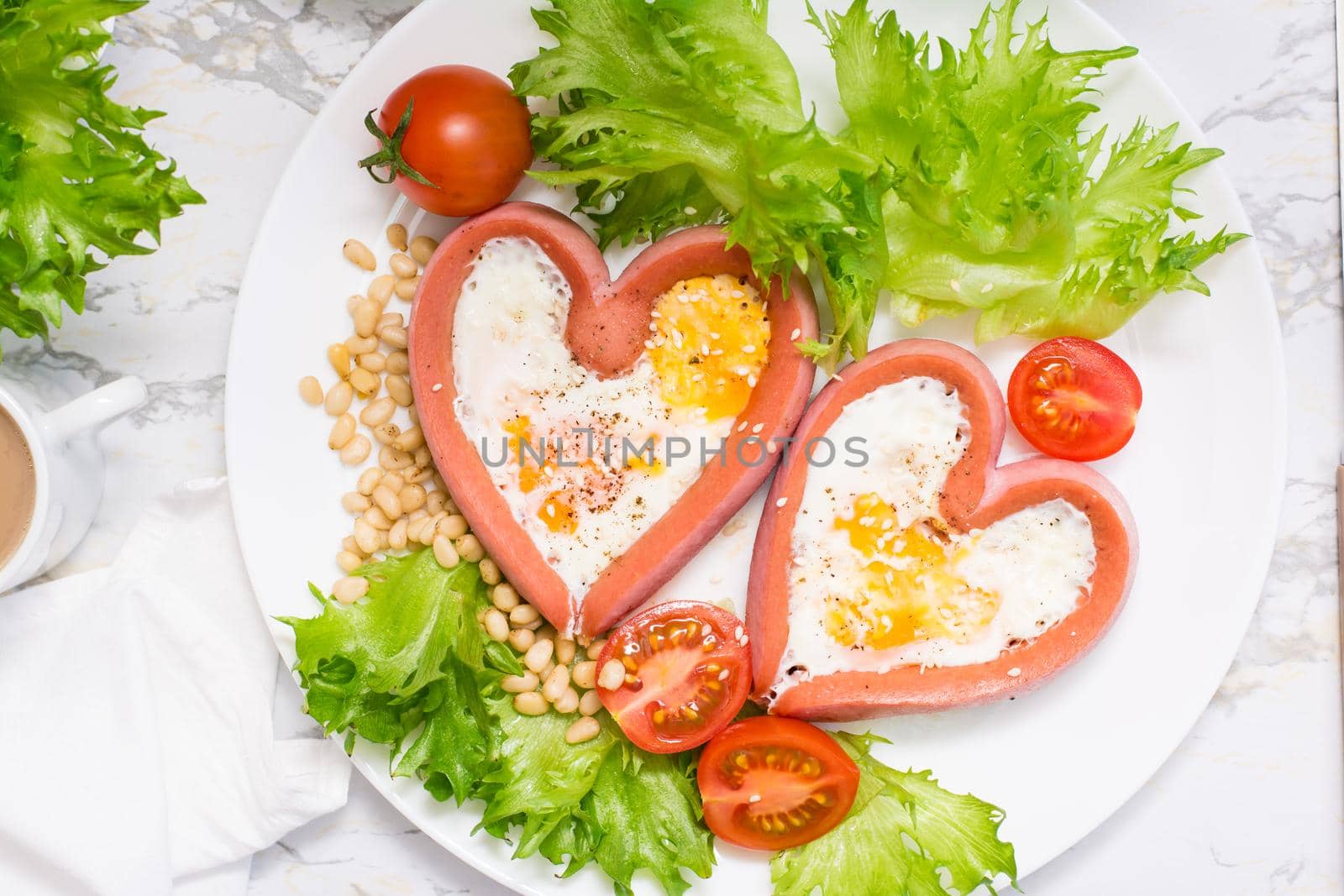 Romantic breakfast. Fried eggs in heart shaped sausages, lettuce and cherry tomatoes on a plate on the table. Top view. Close-up