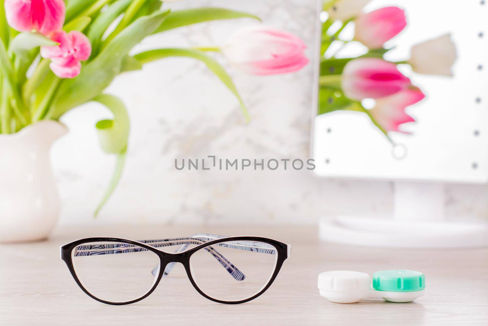 Low vision and the choice between glasses and lenses. A container for lenses and glasses in front of a mirror on the table and a bouquet of tulips in a vase