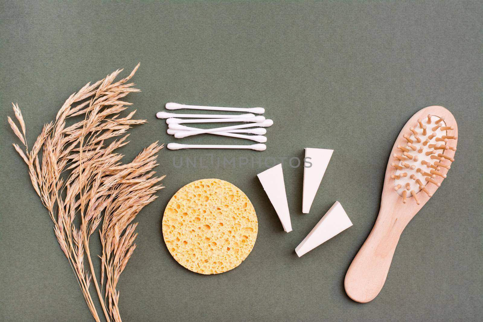 Makeup items. Two types of sponges, cotton swabs, comb and ears of grass on a green background