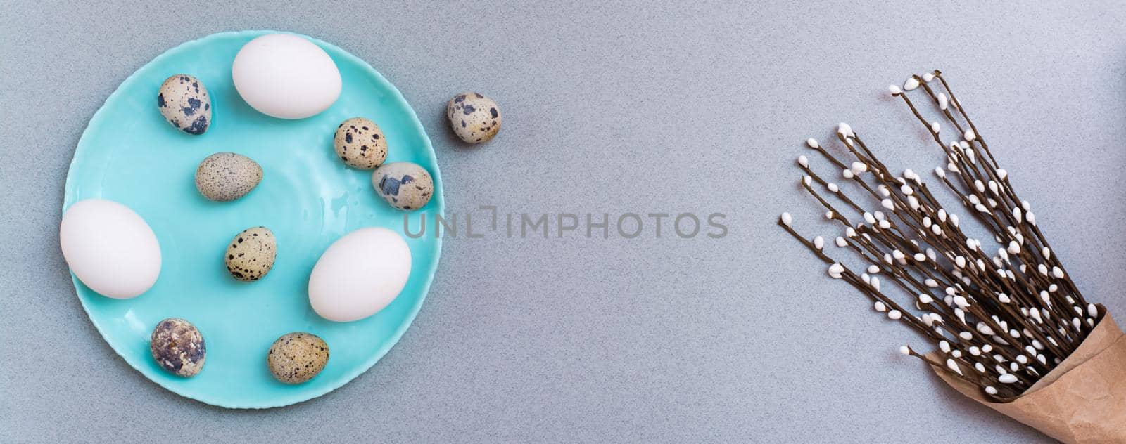 Happy Easter. Chicken and quail eggs on a plate and packaging with pussy willow branches on a gray background. Top view. Web banner by Aleruana