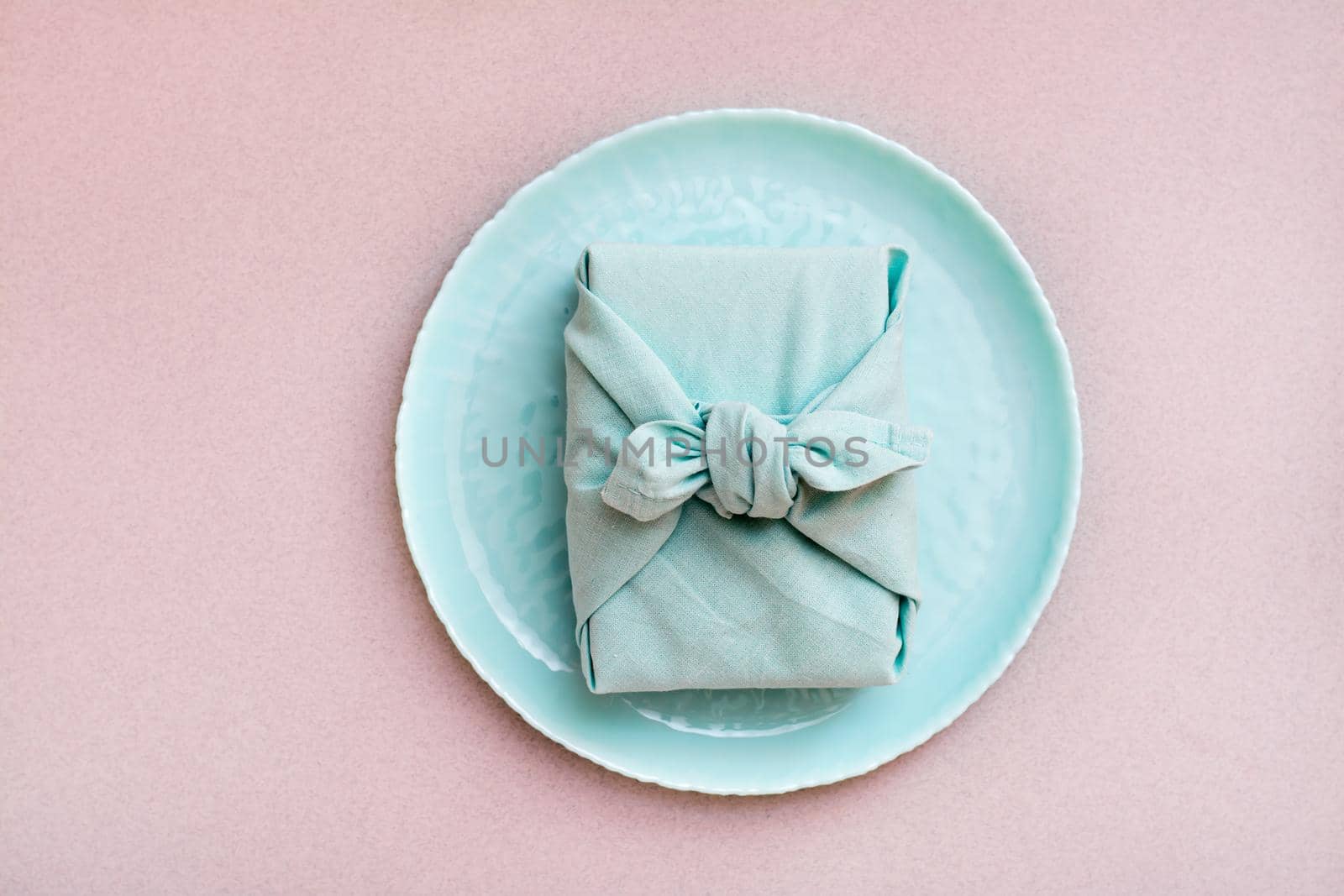 Eco-friendly gift - a box wrapped in cloth on a plate on a gray background. Minimalism by Aleruana