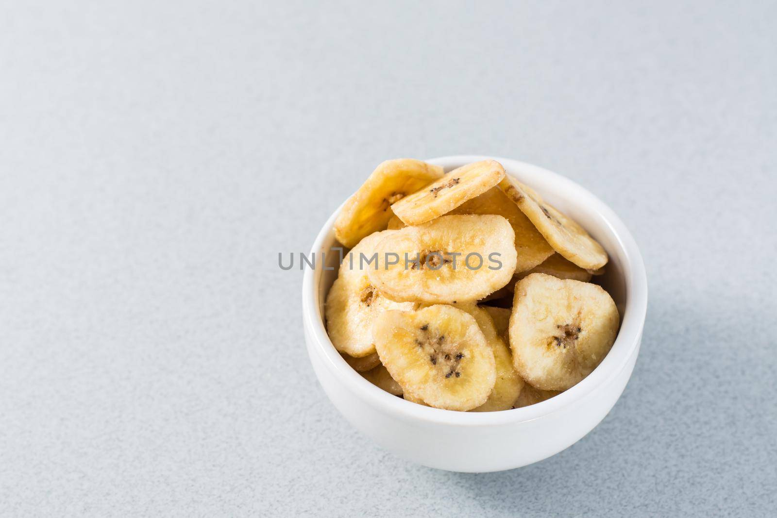 Baked banana chips in a white bowl on the table. Fast food. Copy space by Aleruana