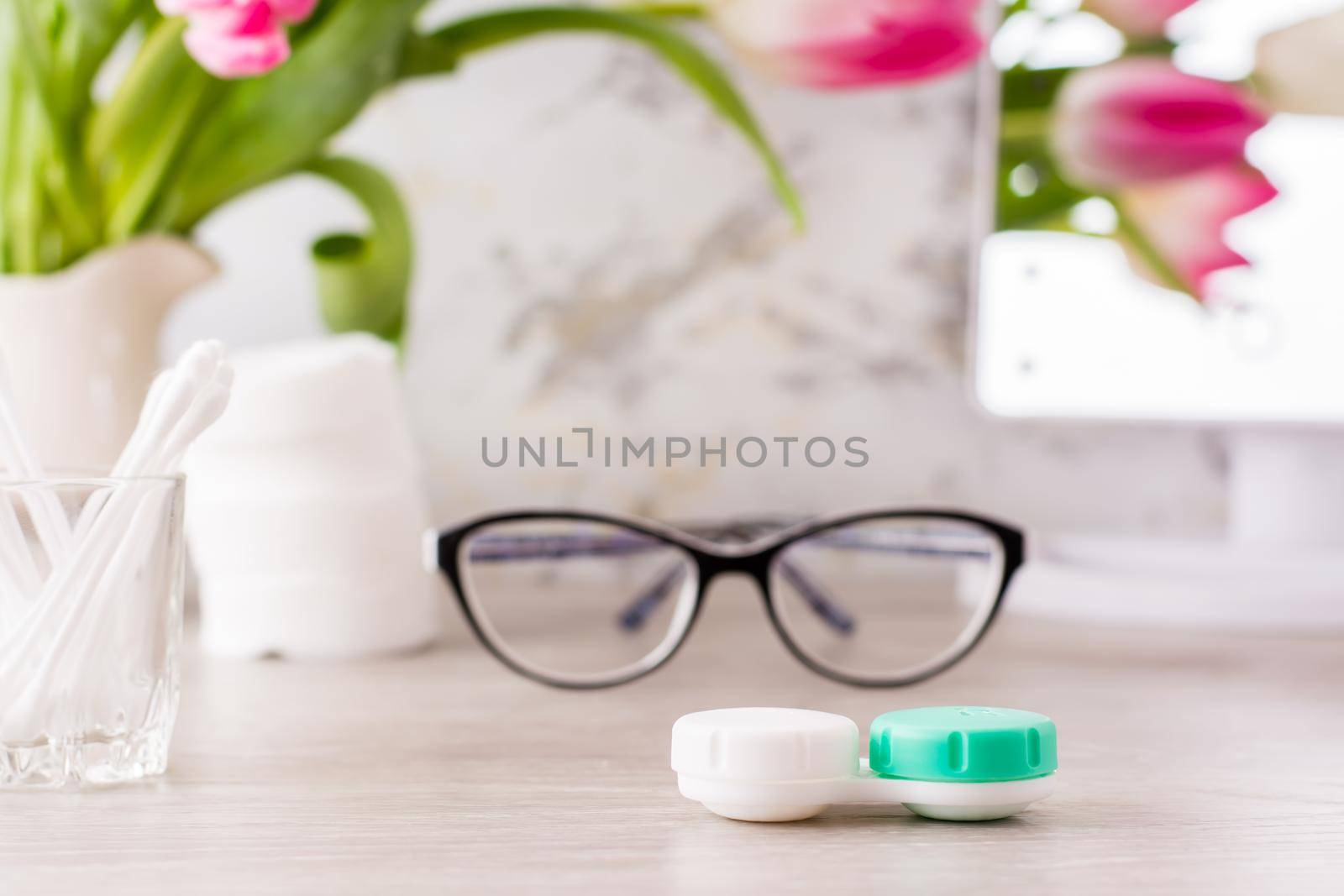 Low vision and the choice between glasses and lenses. Container for lenses on the background of glasses, hygiene products and a mirror on the table by Aleruana