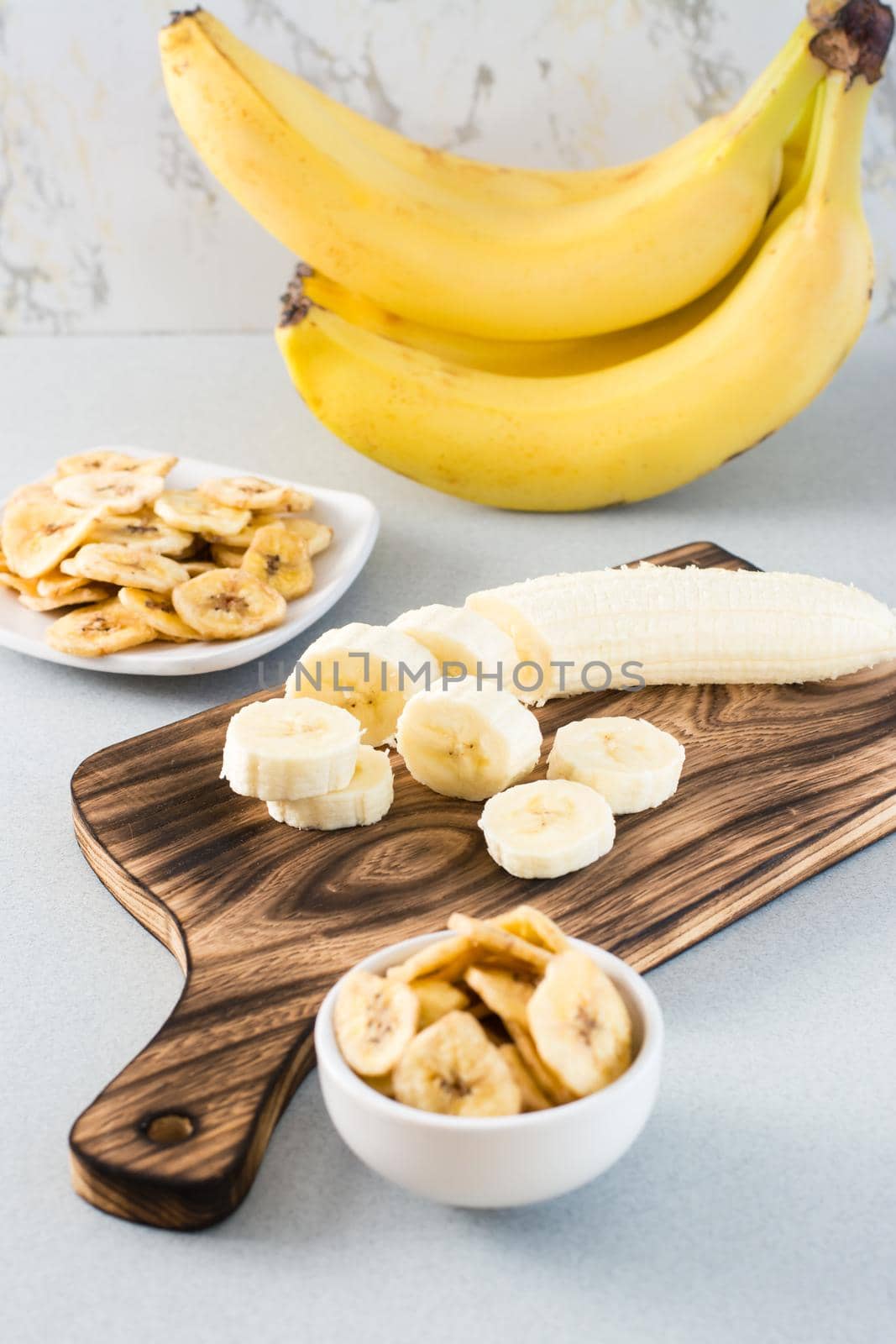 Banana slices on a cutting board and banana chips in a bowl on the table. Fast food.  Vertical view