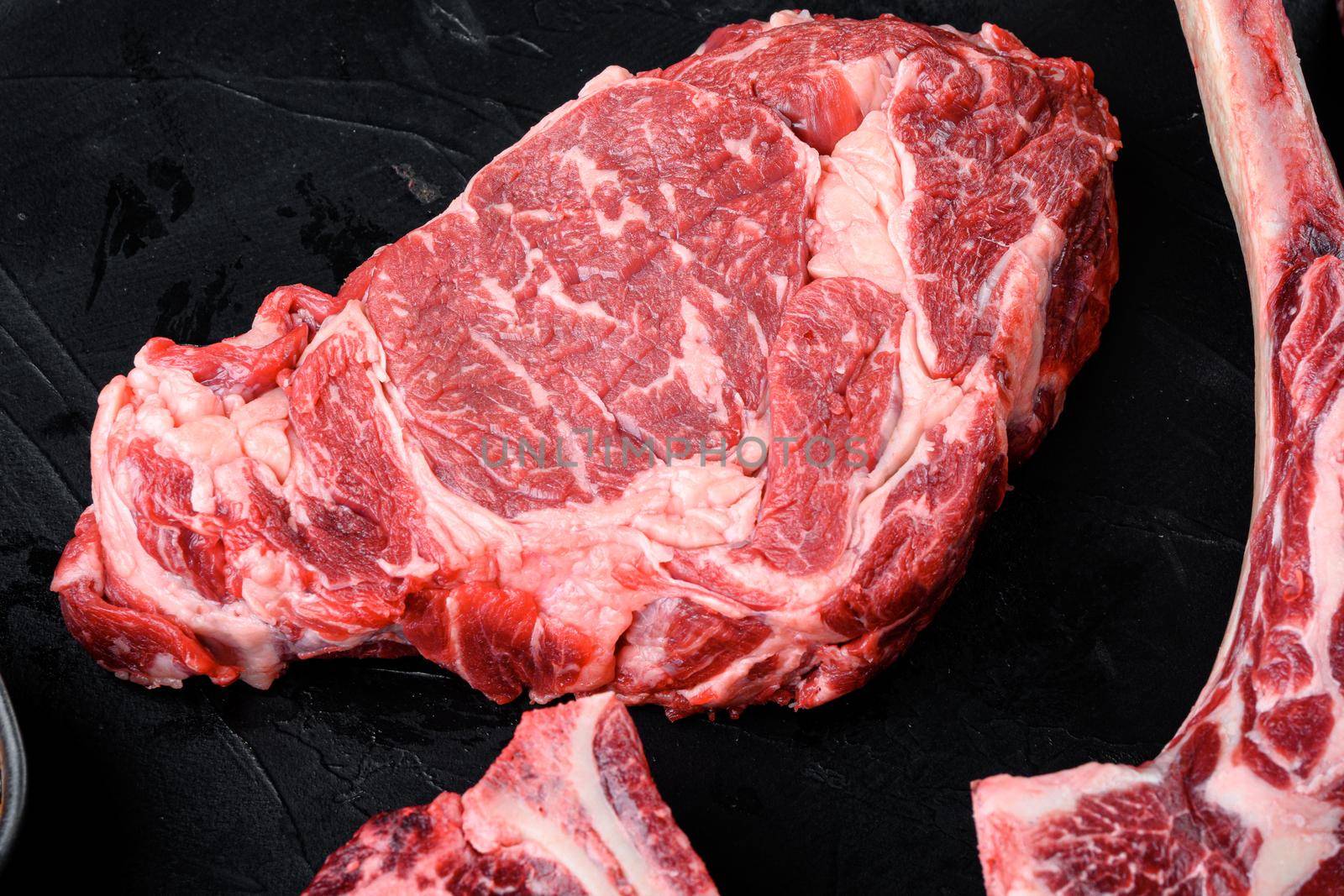 Raw fresh marbled meat Steak Ribeye. Black Angus Rib eye set, on black stone background, top view flat lay