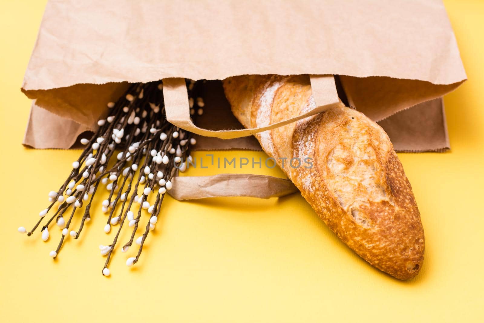 Food delivery concept. Bread and pussy willow bouquet in paper bag on yellow background