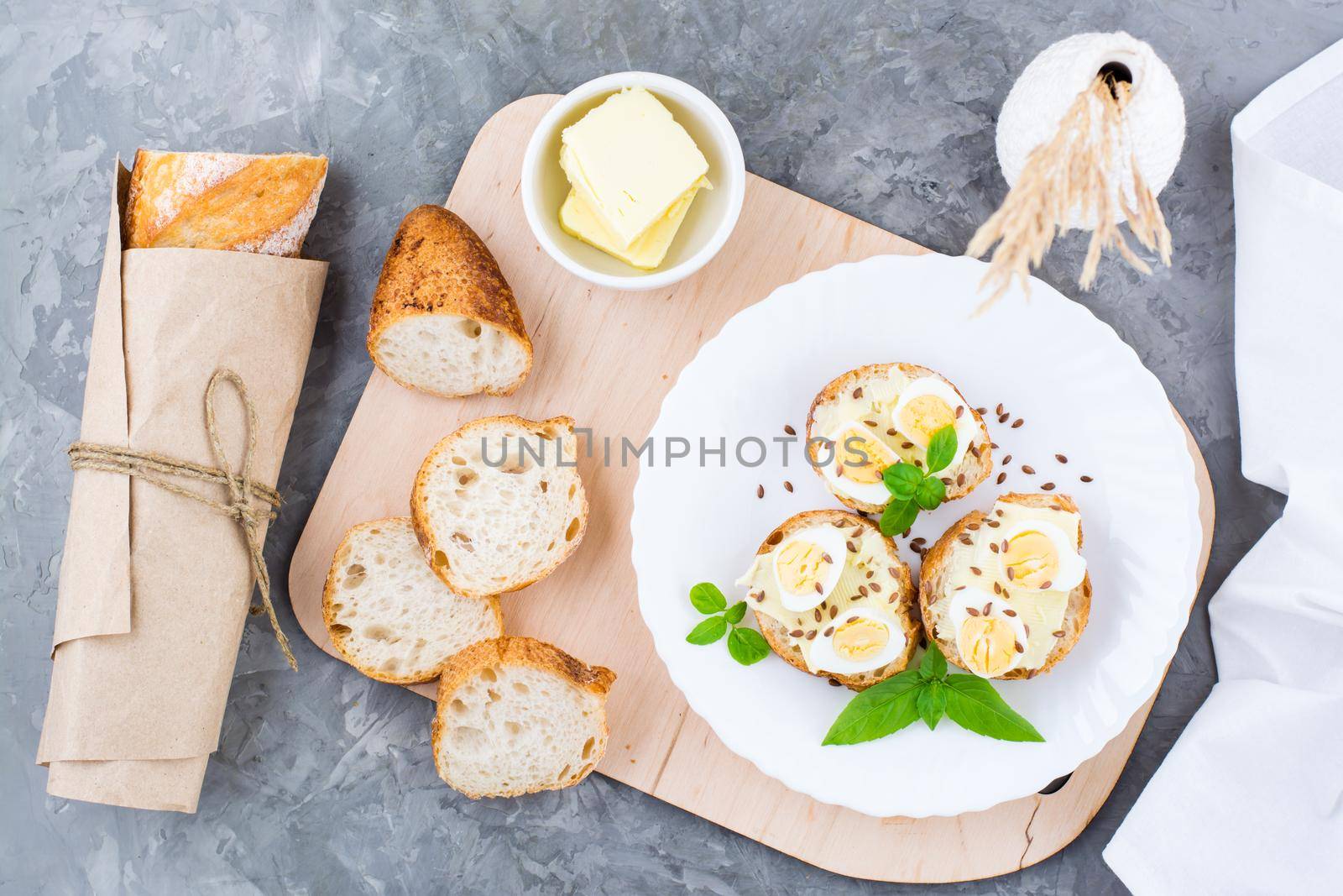 Hearty breakfast in the morning. Fresh baguette sandwiches with butter, quail eggs, flax seeds and basil seeds on a plate on the table. Top view by Aleruana