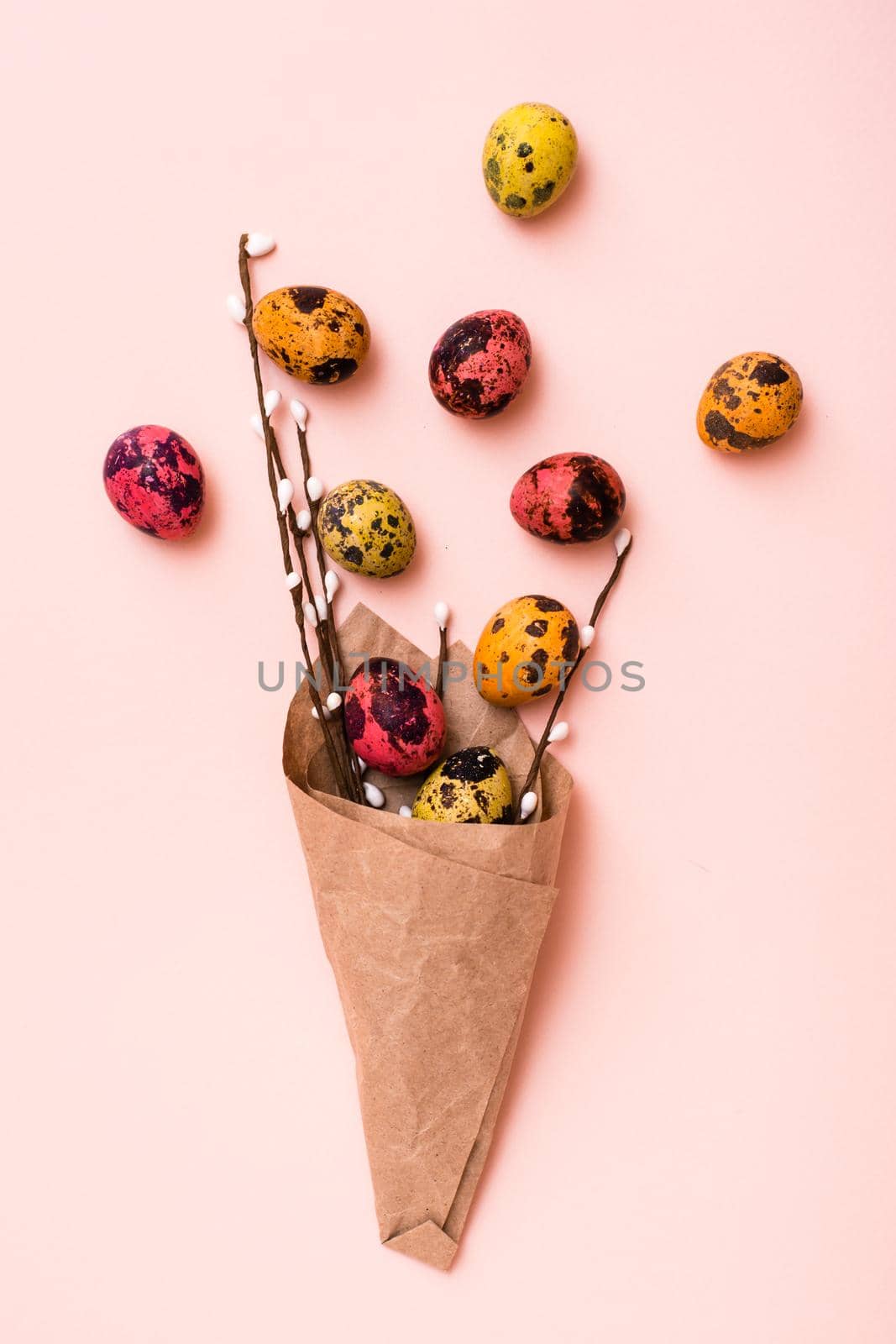 Happy Easter. Bouquet of painted quail eggs and pussy willow branches wrapped in brown paper on pink background. Vertical view