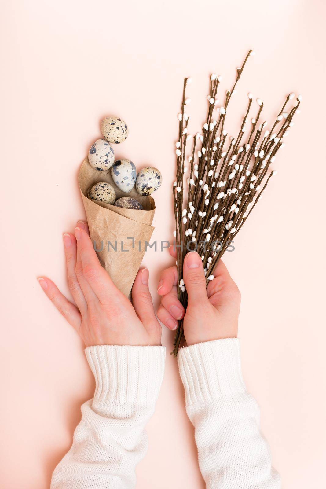Happy Easter. Female hands hold a bag of quail eggs and a bouquet of pussy willow on a pink background