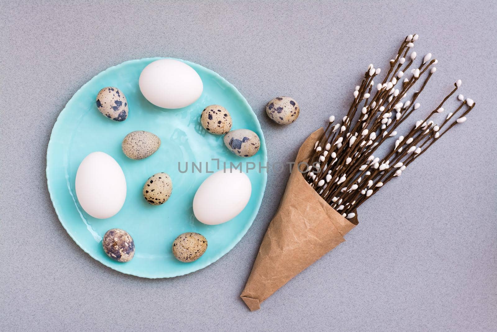 Happy Easter. Chicken and quail eggs on a plate and packaging with pussy willow branches on a gray background. Top view