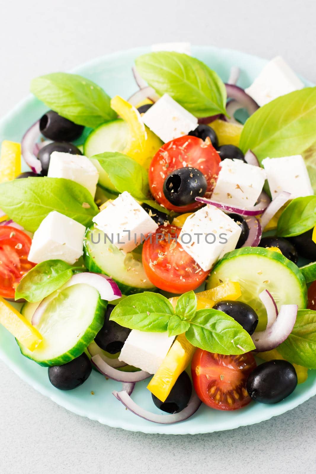 Fresh homemade greek salad with basil leaves on a plate on the table. Domestic life. Vertical view. Close-up
