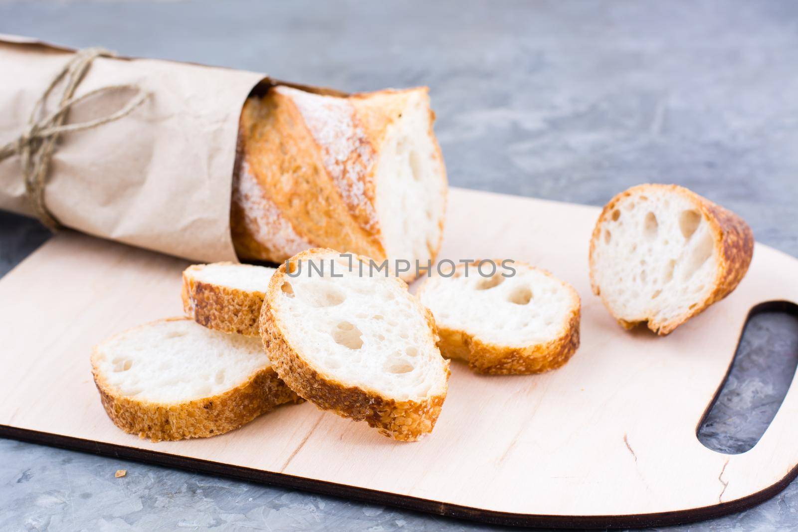 Fresh baguette in wrapping paper cut into pieces on a cutting board on a table by Aleruana