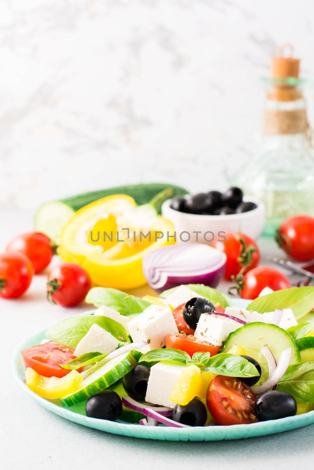 Fresh homemade greek salad with basil leaves on a plate and ingredients for cooking on the table.  Vertical view. Close-up by Aleruana