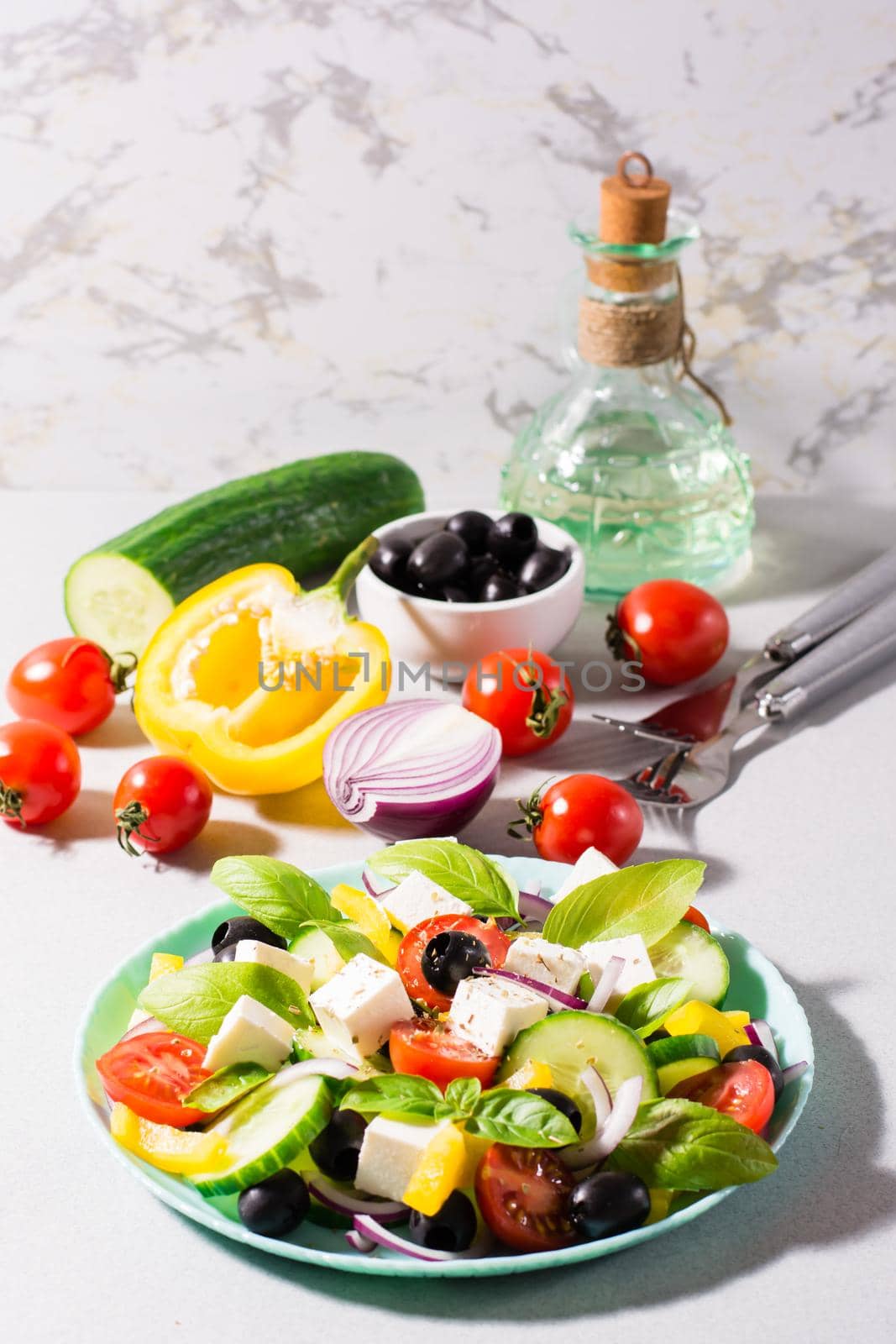 Fresh homemade greek salad with basil leaves on a plate and ingredients for cooking on the table. Domestic life. Vertical view. Hard light by Aleruana